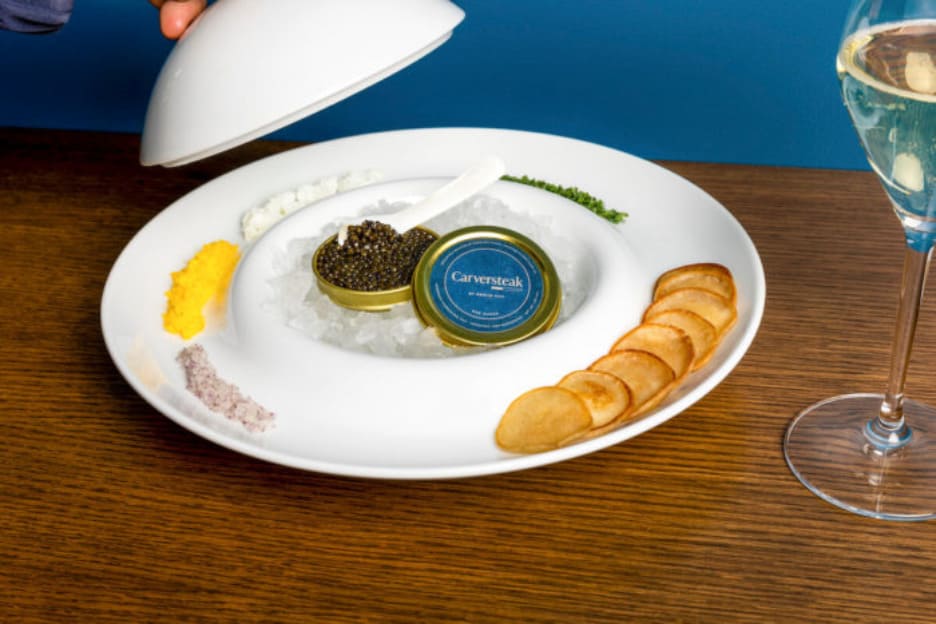 Tin of Carversteak caviar on ice with garnishes, chips, and a glass of champagne.