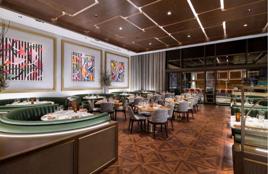 Interior of a modern restaurant with green velvet booths, wood floors, and abstract art on the walls.