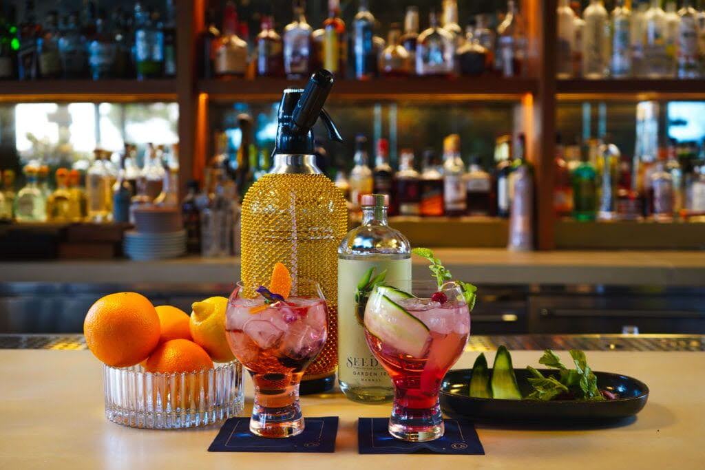 Flanker bar with two signature pink cocktails, fruits, Seedlip bottle, and seltzer