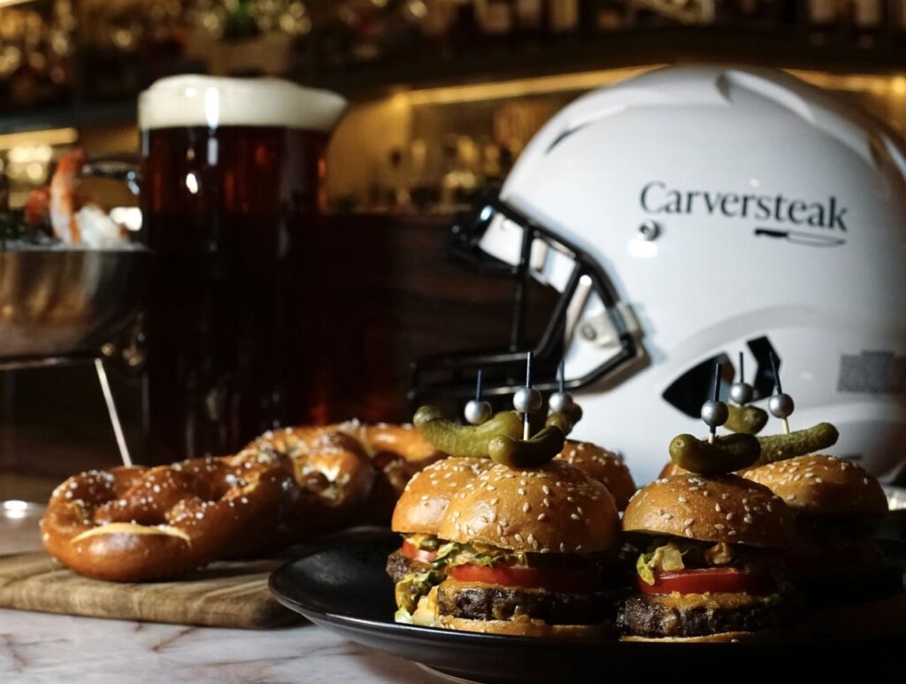 Sliders and pretzels on a bar counter with a football helmet and beer in the background.