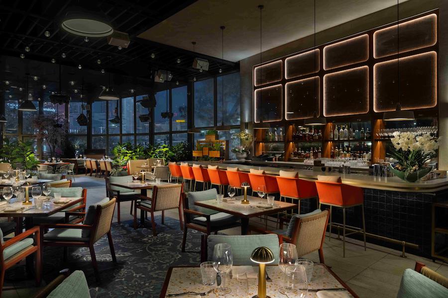 Carversteak dining room featuring elegant table seating, orange bar stools, a full-service bar, and modern ambient lighting.