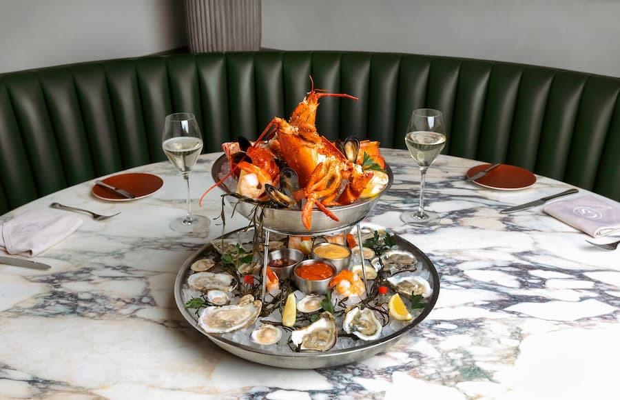 Seafood platter featuring lobster, oysters, mussels, lemon wedges, and dipping sauces served on a marble dining table.